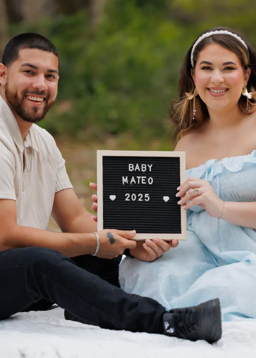 Couple sitting on a blanket, holding a letter board that announces "Baby Mateo 2025" with decorative hearts. Couple sitting on a blanket, holding a letter board that announces "Baby Mateo 2025" with decorative hearts